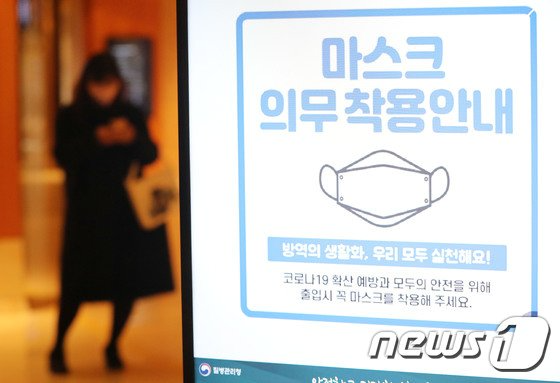 韩国室内口罩义务提示图，背景显示一家医院或公共设施的入口。此图反映韩国政府防疫措施变化。