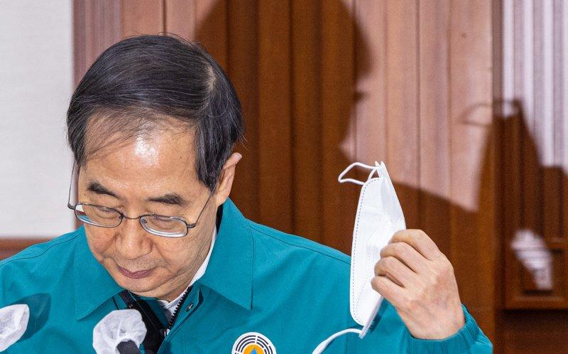 室内マスク着用義務の解除について話す人物の手にはマスクが持たれている。新型コロナウイルス感染症対策会議での様子を収めた写真。