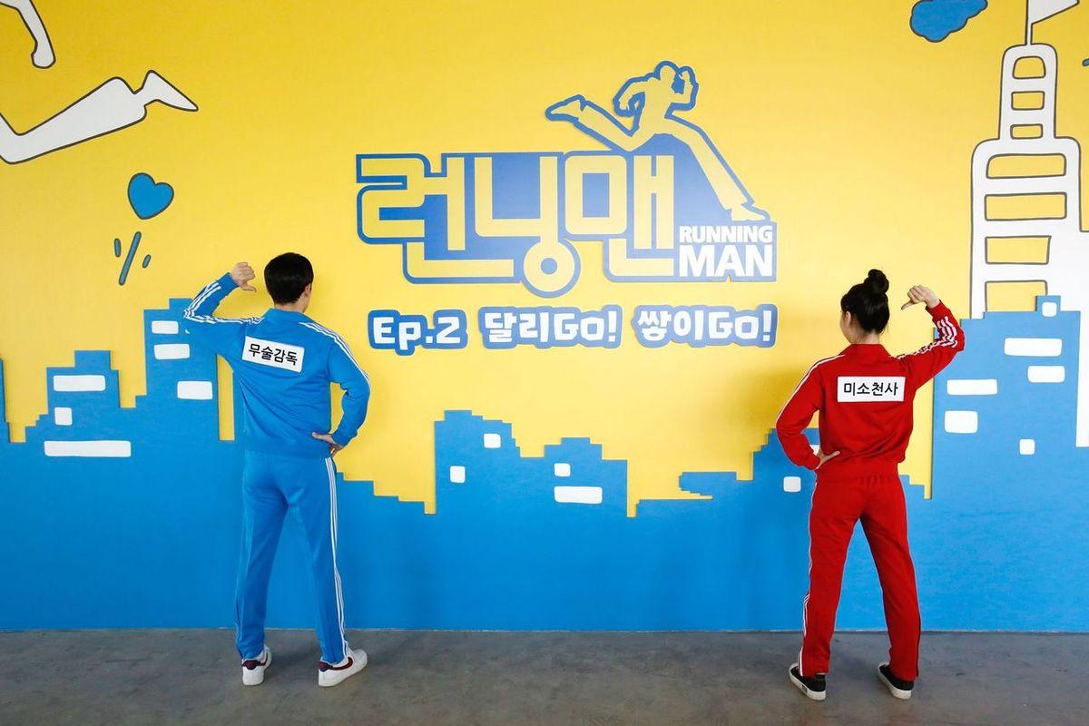 ชายและหญิงในชุดกีฬา กำลังยืนหน้าผนังสตูดิโอของ Running Man Experience Center ที่ปูซานในการเซลฟี่ที่ระลึก หลังเสร็จภารกิจในศูนย์ประสบการณ์ Running Man Experience Center ที่ปูซาน ประเทศเกาหลีใต้