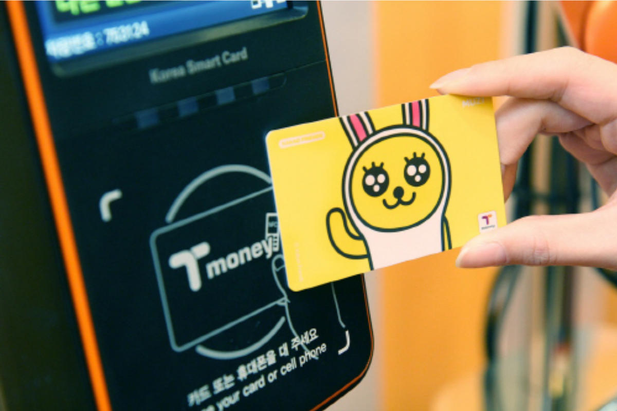 用韓國Tmoney交通卡進出巴士或地鐵時需刷卡。Tmoney卡在支付終端輕觸進行付款，特寫展示黃色的韓國旅遊卡與支付機。韓國旅遊卡是公車與地鐵等交通工具的便捷支付方式。