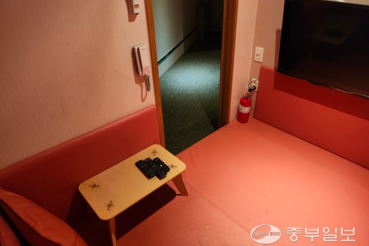 Bên trong một phòng ở Room Cafe tại Hàn Quốc với ghế sofa màu đỏ và bàn nhỏ, có màn hình TV và điện thoại treo tường.