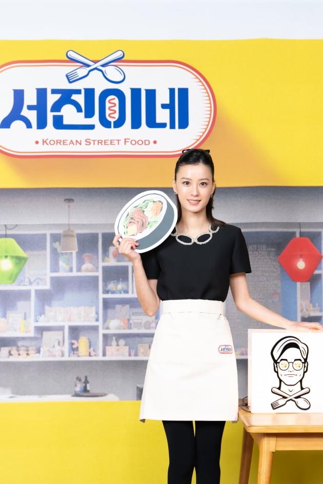 黒い服を着た人物が、サムギョプサルの絵が描かれたファンを持ちながら、tvN「ソジンの家」のロゴ前でポーズしている。