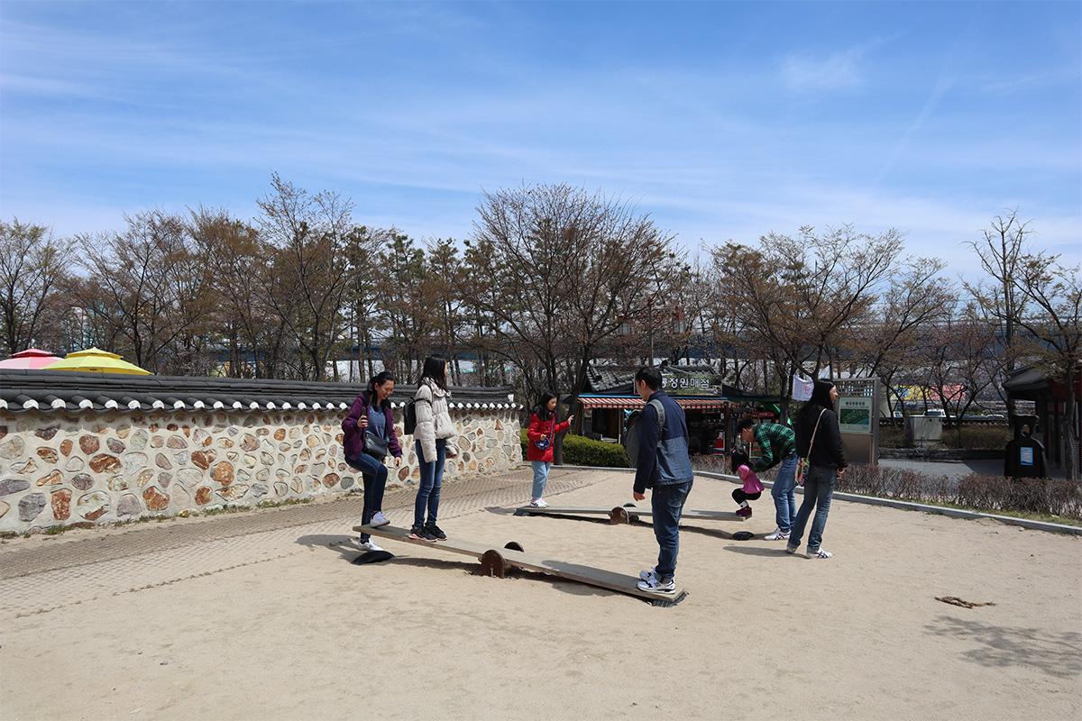 A visit to Wolmido amusement park with attractions like ferris wheels and thrill rides, complemented by blossoming cherry trees.