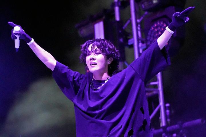 J-HOPEがアメリカ、シカゴのグラントパークでのロラパルーザ音楽フェスティバルのステージで、観客に向けて両手を広げている姿。