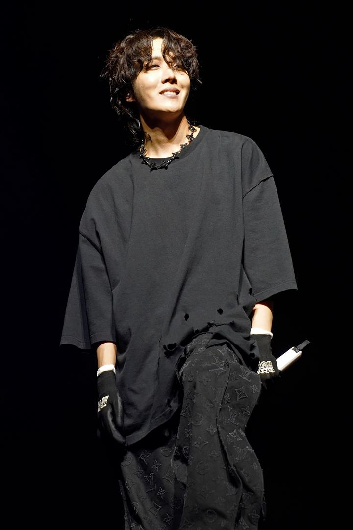BTSのメンバー、J-HOPEがアメリカの音楽フェスティバル「ロラパルーザ」でのソロ公演中に暗い舞台でカジュアルな黒い服装をしている姿。