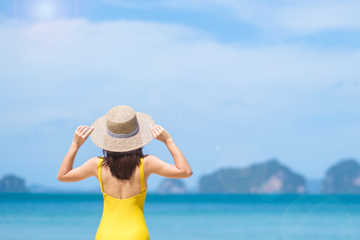 ผู้หญิงในชุดว่ายน้ำสีเหลืองบนชายหาด มองออกไปยังทะเลและท้องฟ้าที่มีแดดจ้า