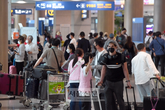 仁川國際機場入境大廳,旅客在搭著手推車通過海關,背景顯示機場指示牌和忙碌的人群。