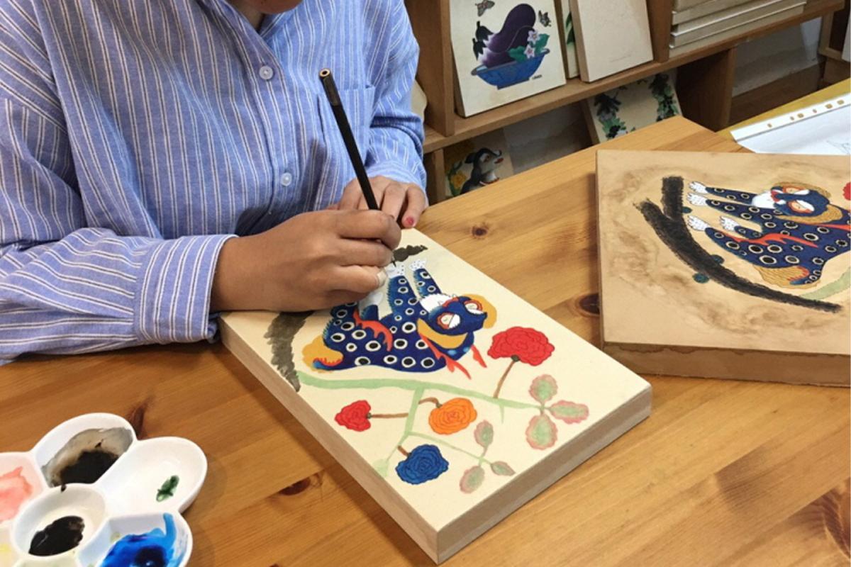 Proses menggambar karya seni minhwa Korea tradisional dengan detail yang teliti.