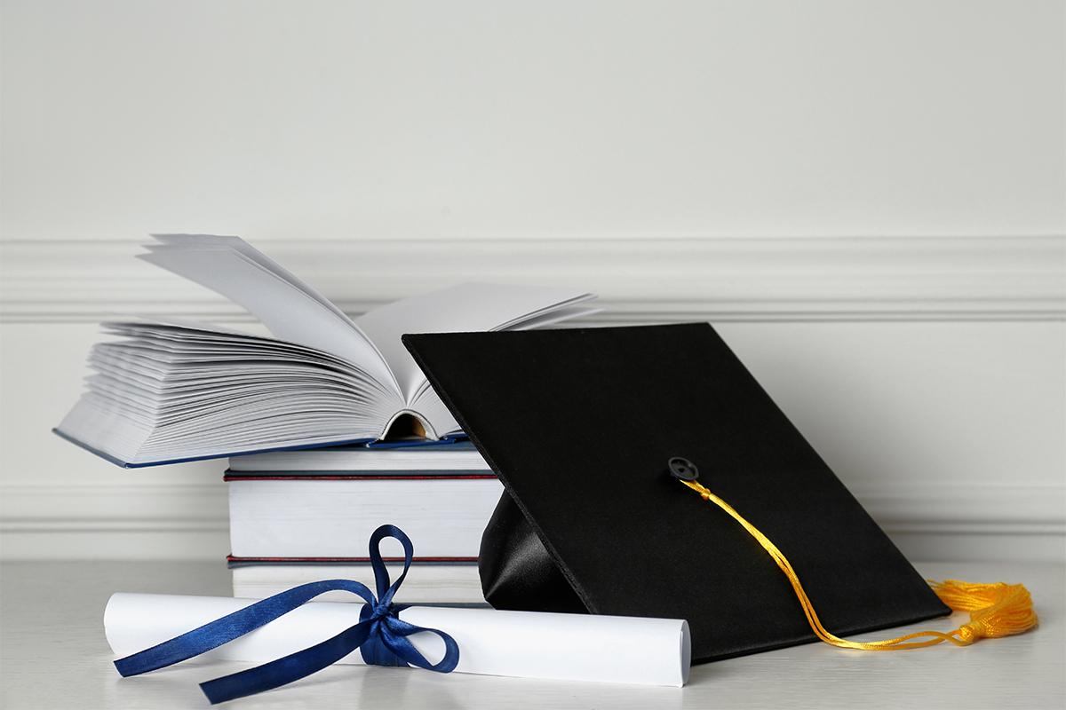 Ein Stapel von Büchern, ein Abschlusszertifikat und ein Doktorhut als Symbol für akademischen Erfolg.
