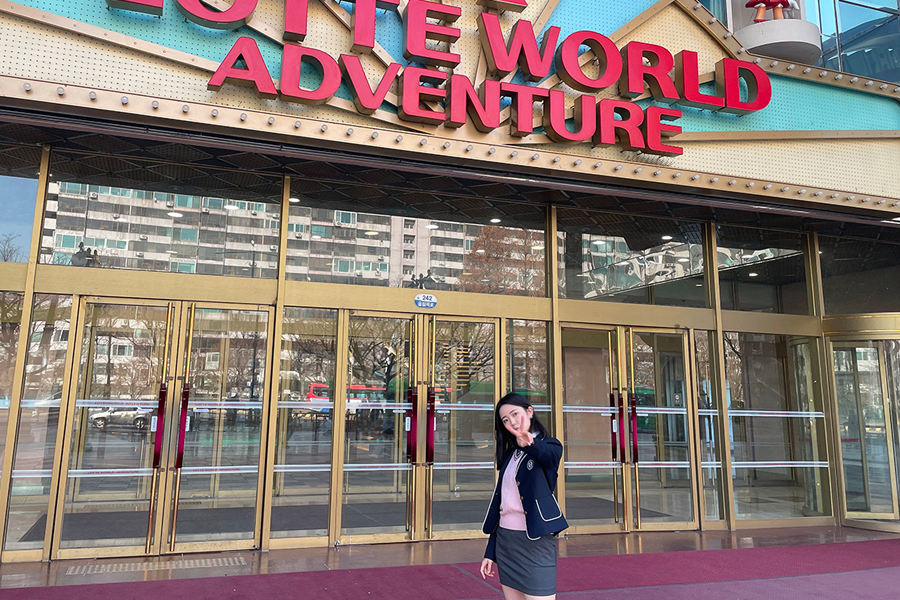 롯데월드 어드벤처 입구 앞에서 촬영된 교복을 입은 사람이 있는 사진.