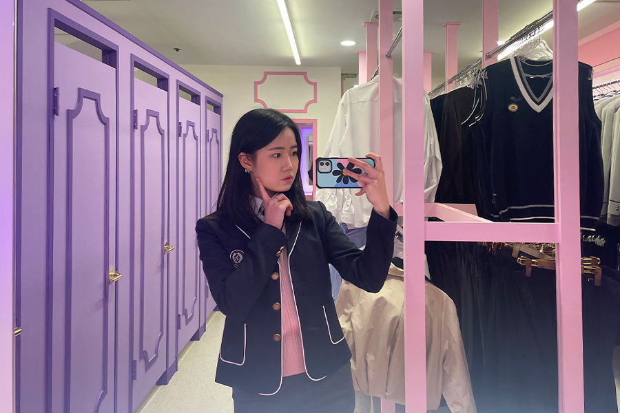 강남교복 대여점 내 거울 옆에 서 있는 사람의 스마트폰 셀카 사진.