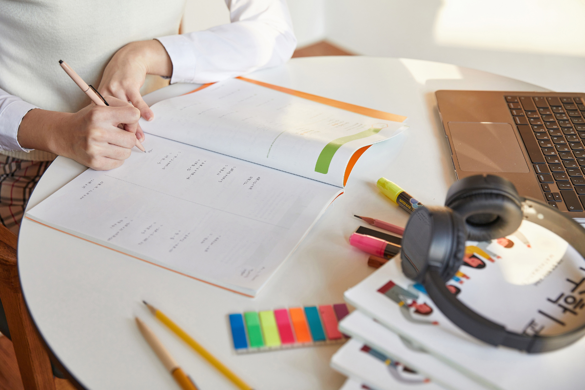 นักศึกษากำลังทำการบ้านภาษาเกาหลีบนโต๊ะ พร้อมอุปกรณ์การเรียนต่างๆ