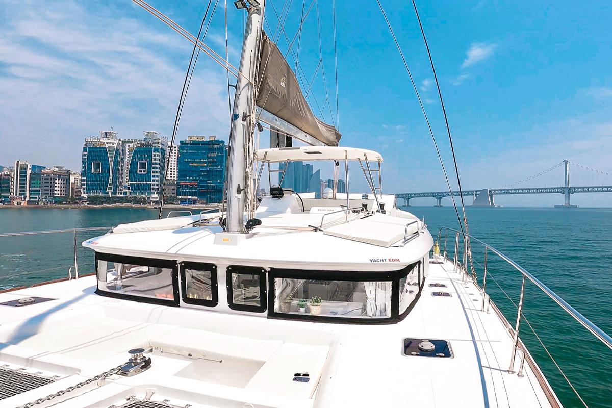 Luxurious yacht deck with modern buildings and Gwangalli Bridge in the background on a sunny day.