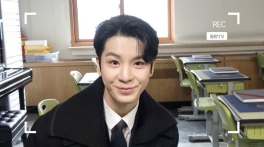 教室で撮影されたスーツ姿の男性、学生の制服を着ている