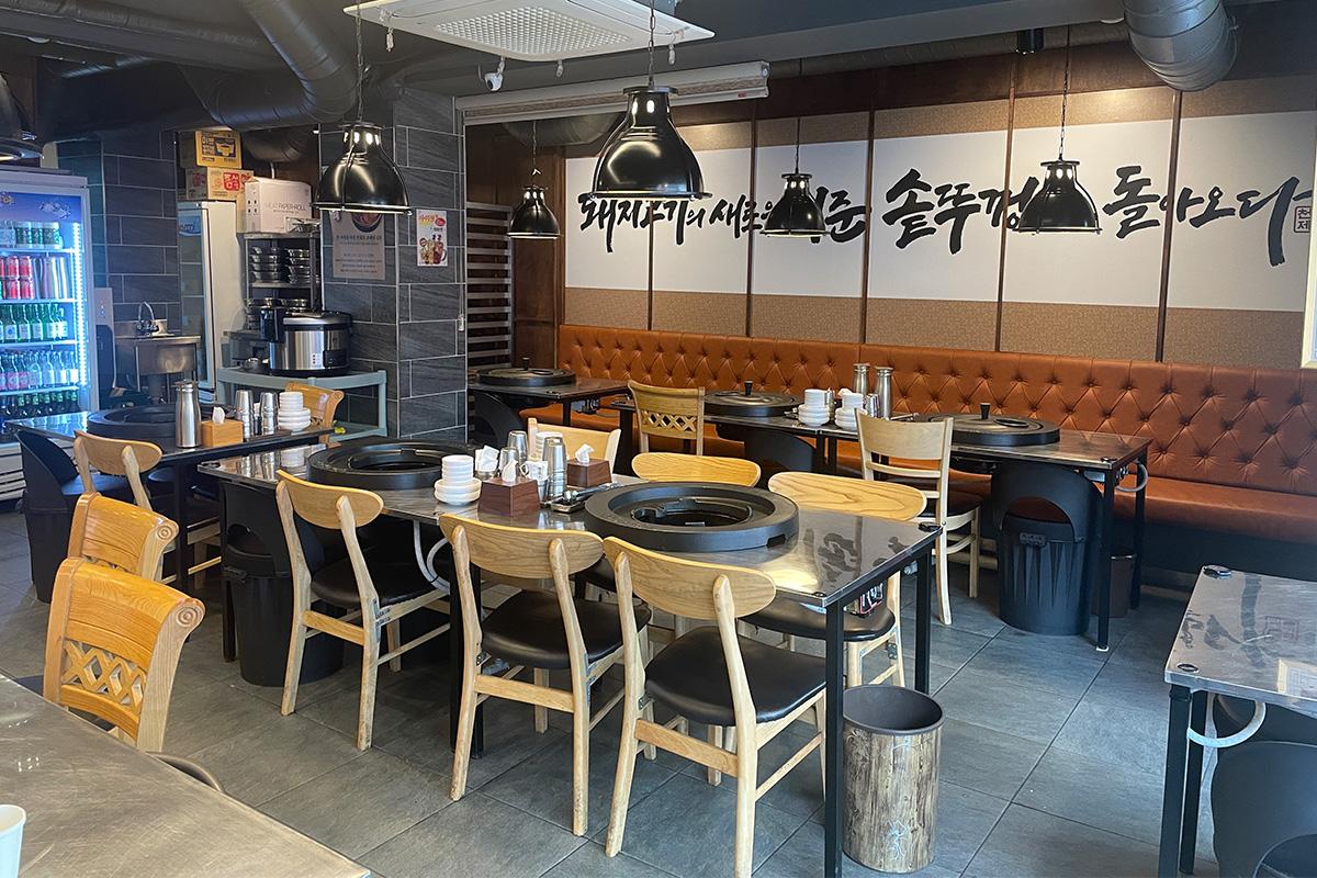 韩国明洞烤肉店，内部环境整洁，木制桌椅和铁锅盖烤盘营造出传统韩式风格