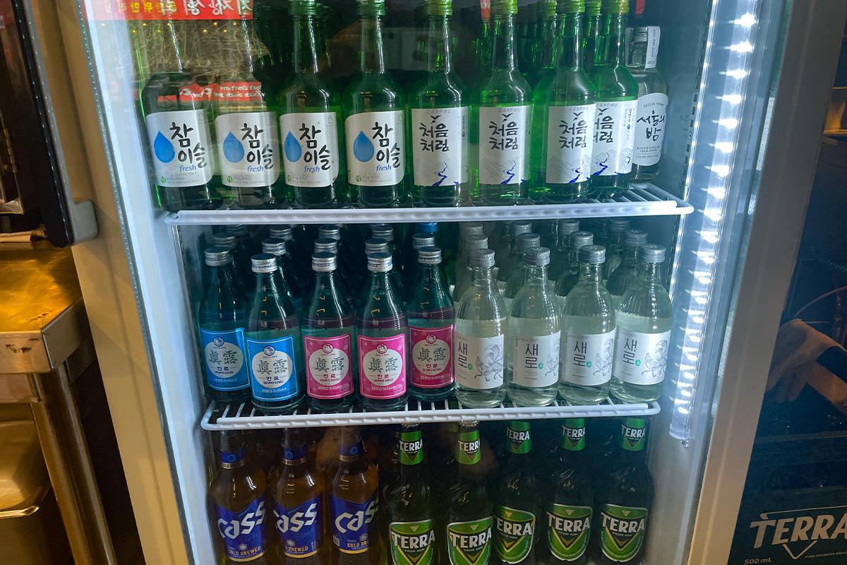 韩国明洞烤肉店的冰箱，陈列了多种韩国传统酒类和饮品，包括烧酒和啤酒