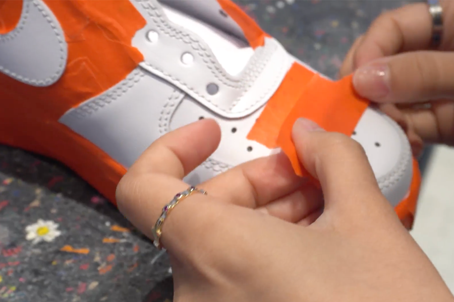 Hands carefully applying tape on a white sneaker during Nike customization