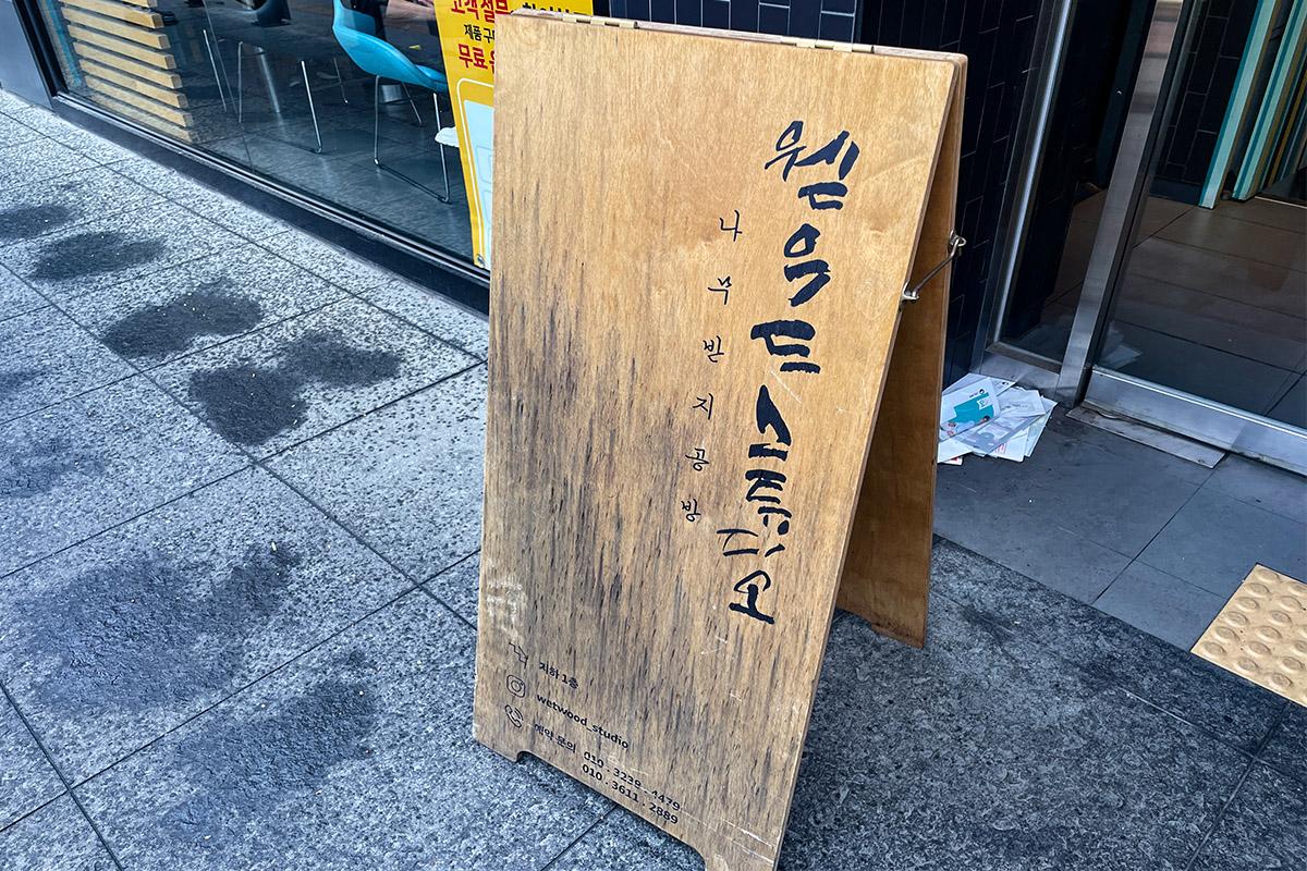 Wetwood Studio 蚕室店外观的木制招牌，刻有工作室名称与联系信息，位于首尔街道。