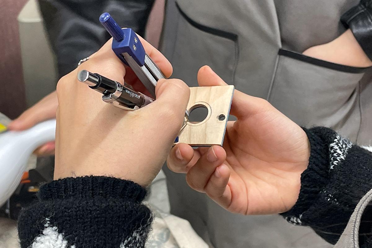 Wetwood Studio 顾客使用圆规在木材上画出所选戒指的宽度，工作人员陪同确保准确度。