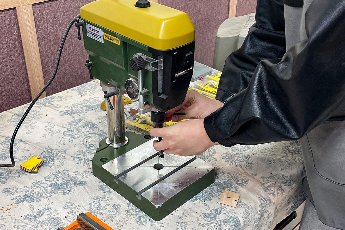 在Wetwood Studio 使用钻床钻孔的顾客，由工作人员协助完成，细致处理木材。