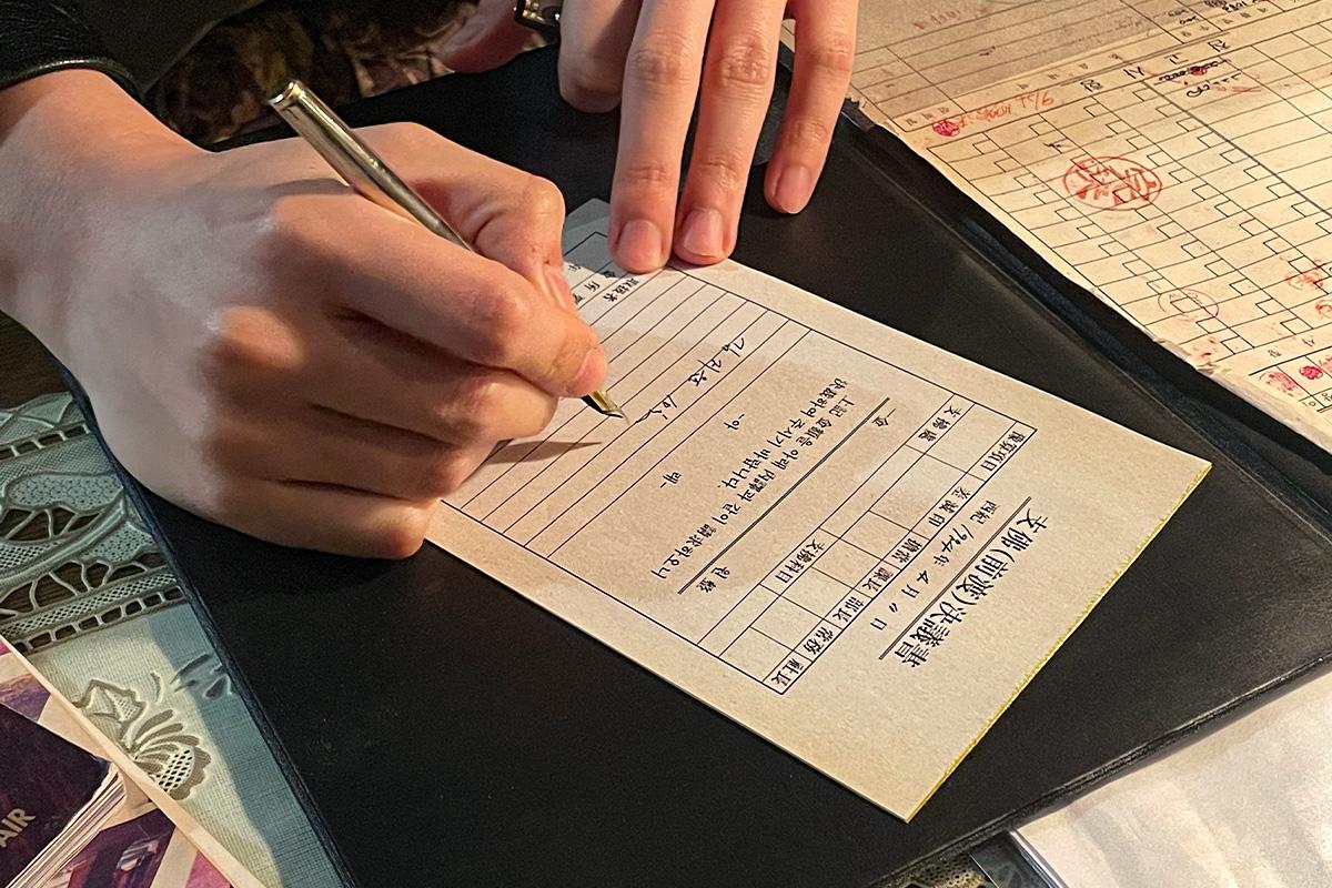 Wetwood Studio 顾客正在使用钢笔填写复古风格的批准书，为木戒指DIY体验做准备。