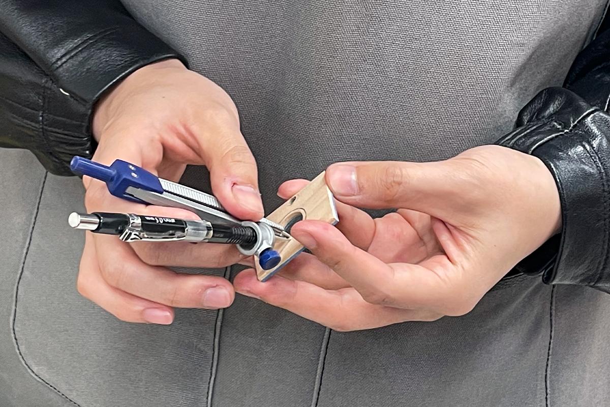 顾客在Wetwood Studio 使用圆规和笔在木材上画圈，规划木戒指设计的轮廓。