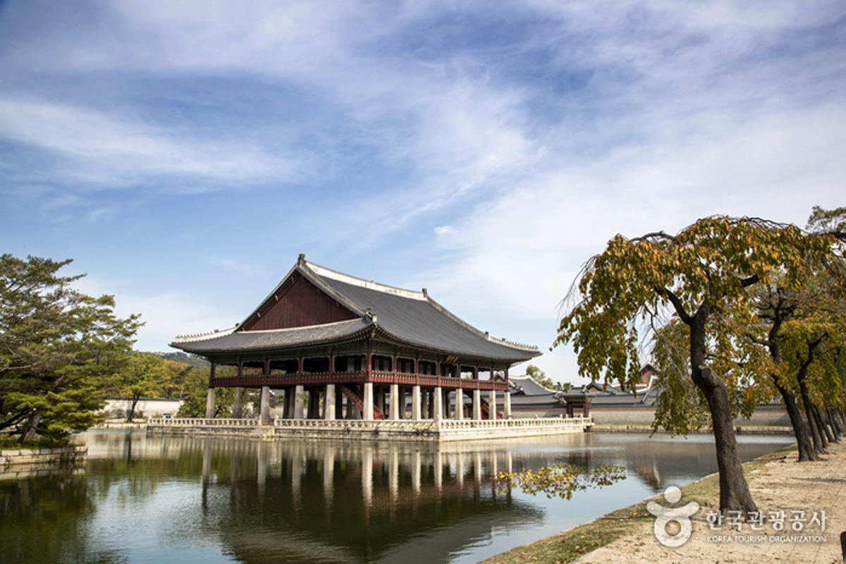 Gedung Pavilion Gyeongbok di Istana Gyeongbokgung dengan refleksi di air kolam pada hari cerah.