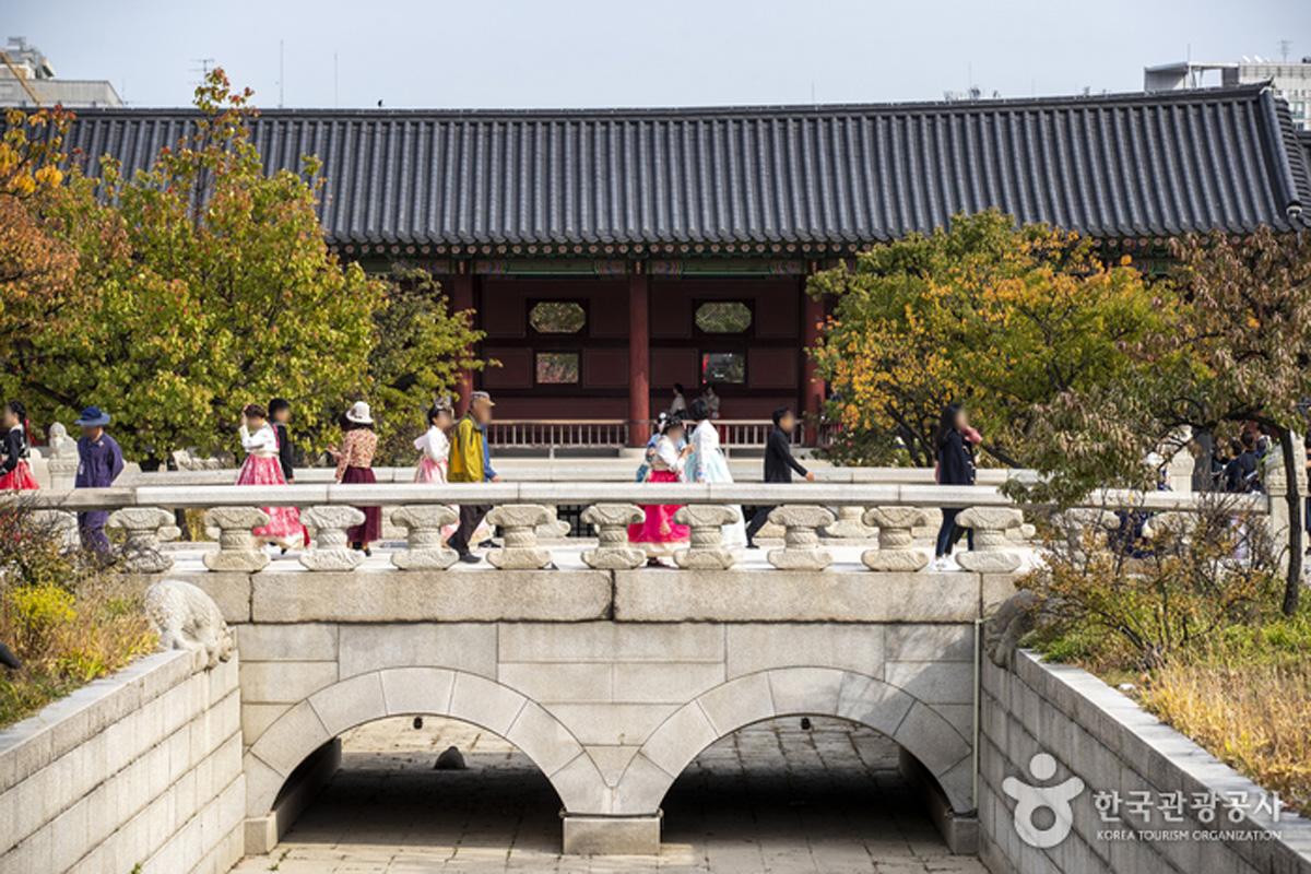 Pengunjung berjalan melewati jembatan di dalam kompleks Istana Gyeongbokgung, beberapa mengenakan hanbok.