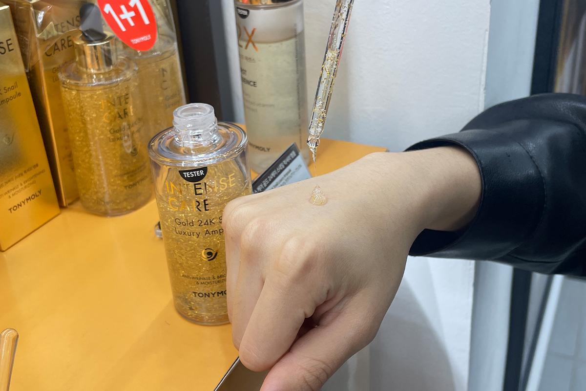 24K Snail Luxury Ampoule-г туршиж байгаа гарын дундах жижиг алтлаг хэсгүүд.