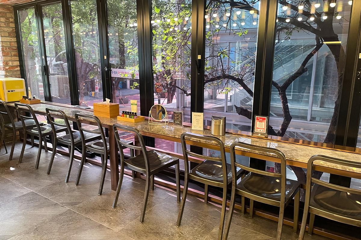 美容沙龍內的待客休息區,設有長桌和椅子,窗外可見街景。