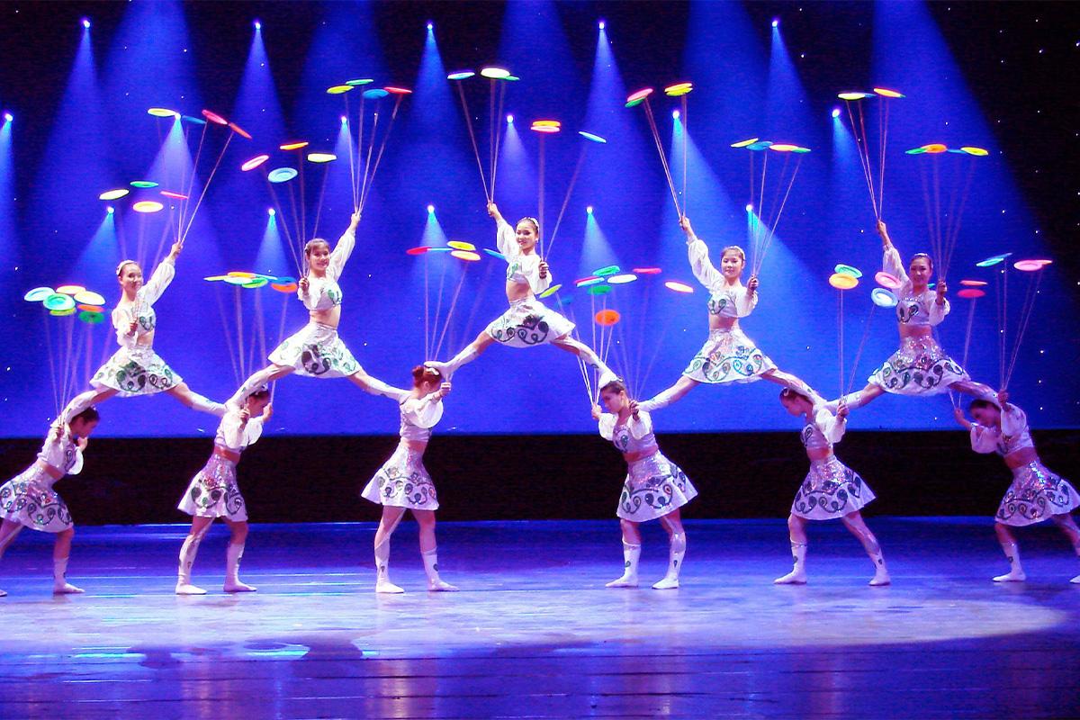 Actuación en el escenario del Circo Dongchun con artistas sosteniendo platos sobre varas bajo luces azules.