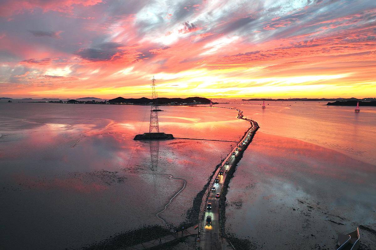 Camino expuesto en la Isla Jebudo al atardecer, conocido como el 'milagro de Moisés', con un cielo naranja.