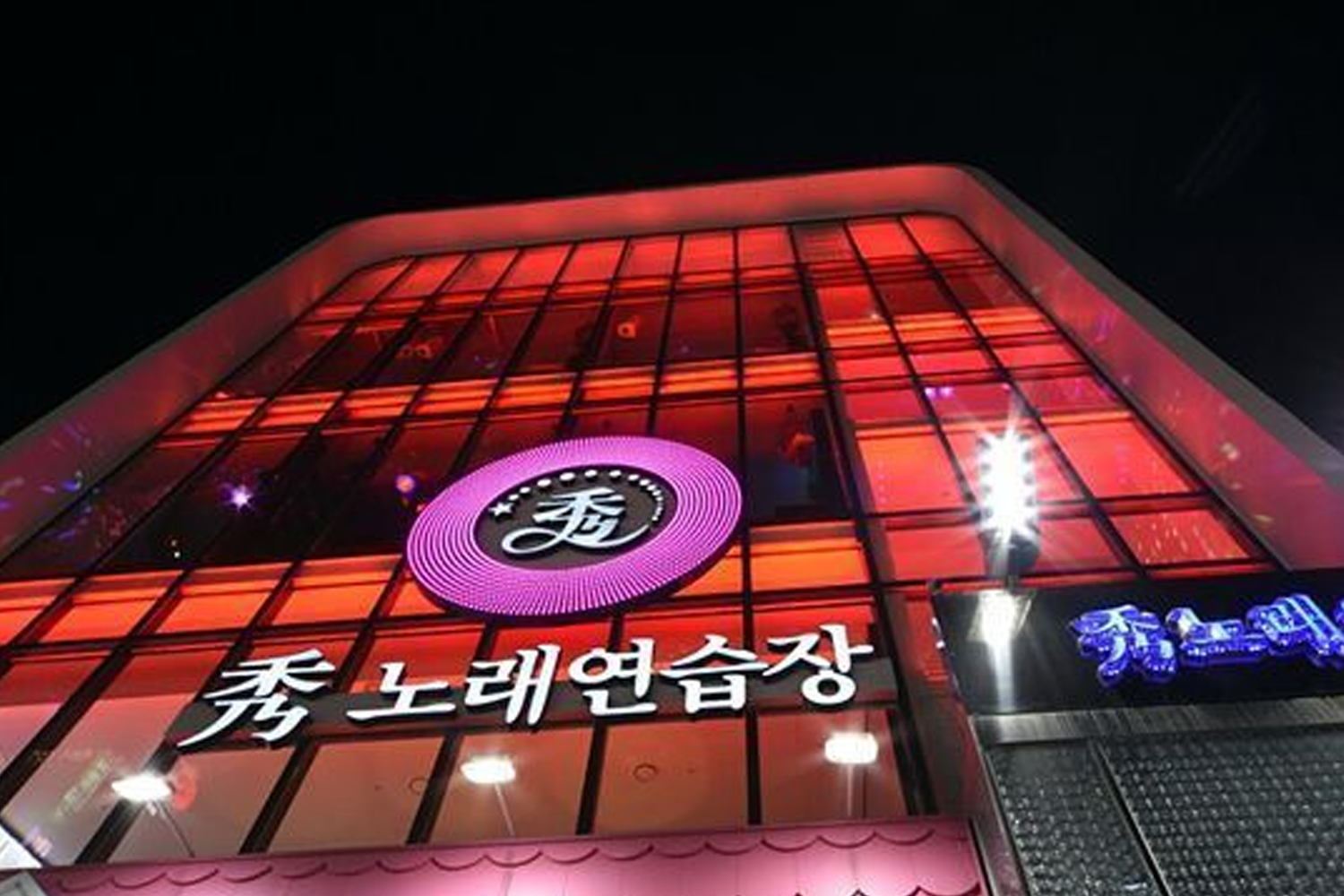 Exterior view of a Korean karaoke building illuminated at night, showcasing its bright and inviting entrance.