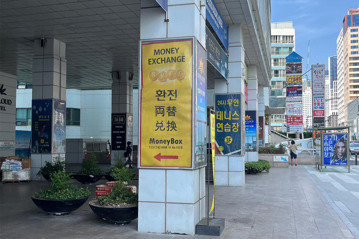 Money Box signage on a building pillar directing towards the currency exchange branch entrance.