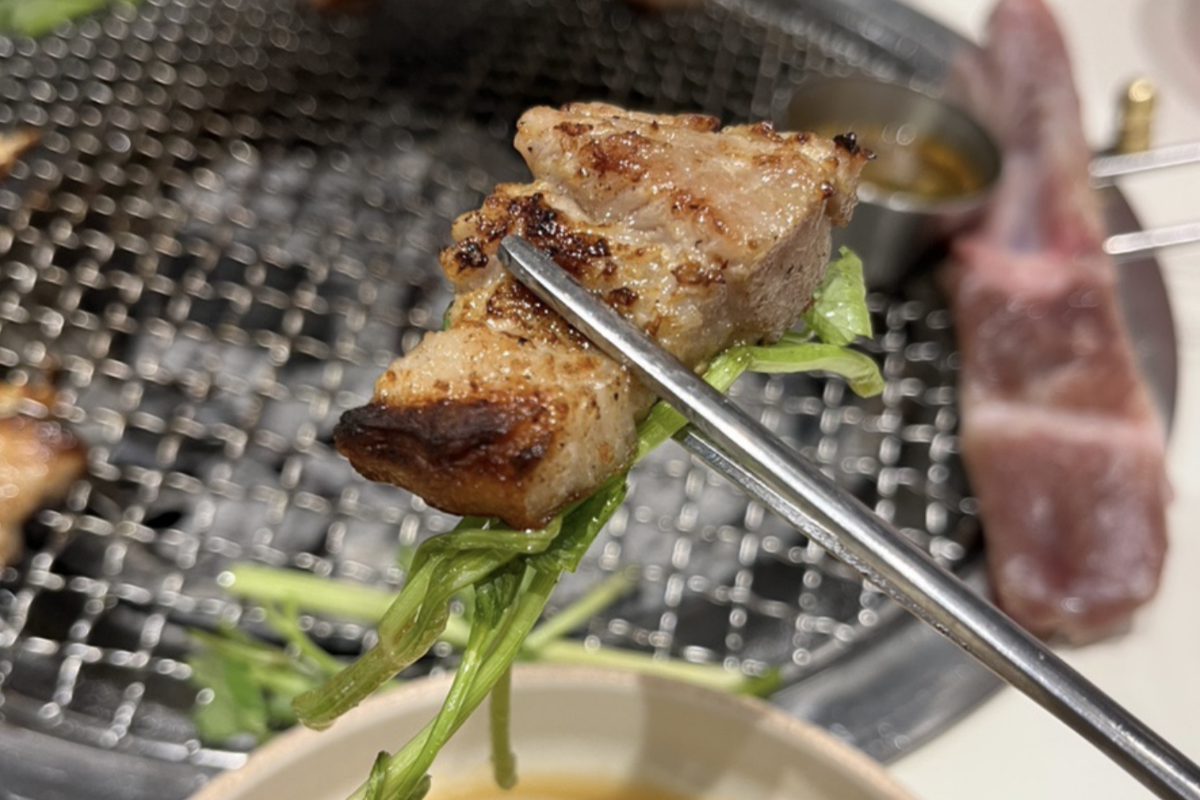 Un trozo de carne samgyeopsal sobre perejil de agua al lado de la parrilla de Dadokine, Hapjeong.