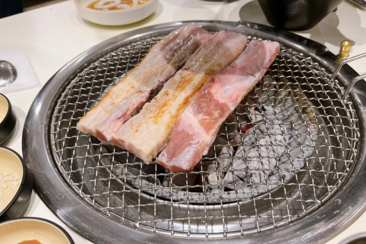 Imagen de tiras de samgyeopsal (panceta) asadas sobre parrilla de carbón en Dadokine, Hongdae.