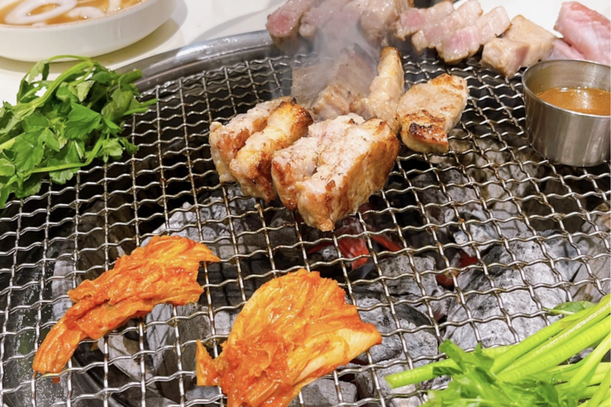Carne samgyeopsal cocinándose con kimchi sobre parrilla de carbón en barbacoa Dadokine, Hongdae.