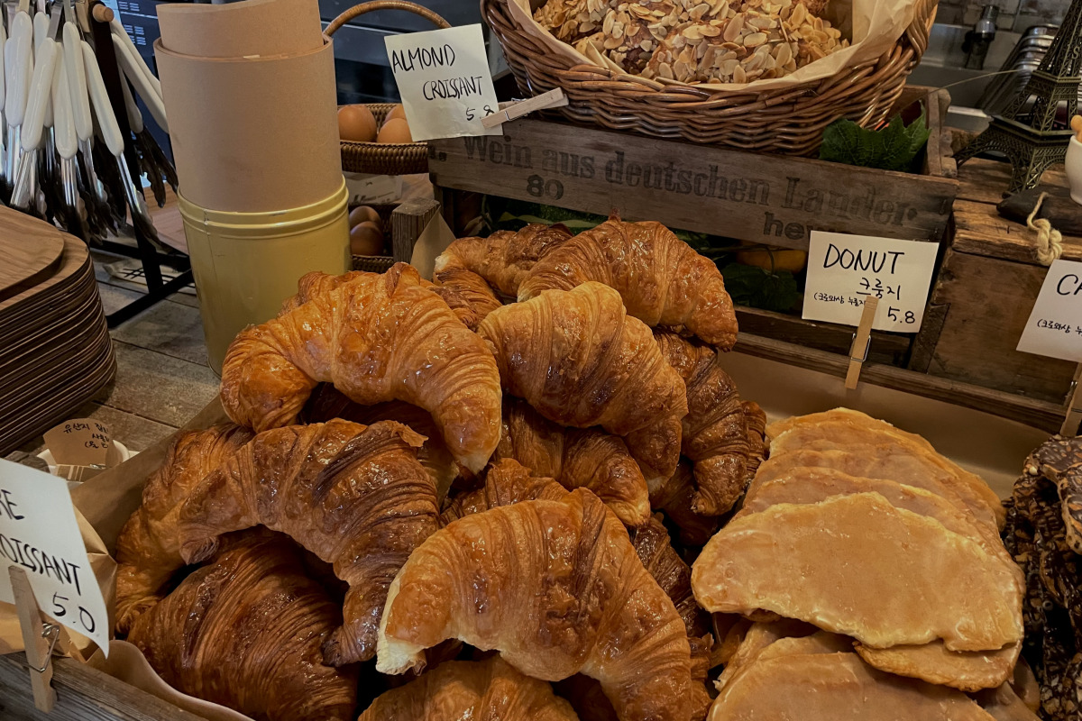Una pila de crujientes croissants y donuts dispuestos para la venta en Teddy Beurre House con etiquetas de precios visibles.