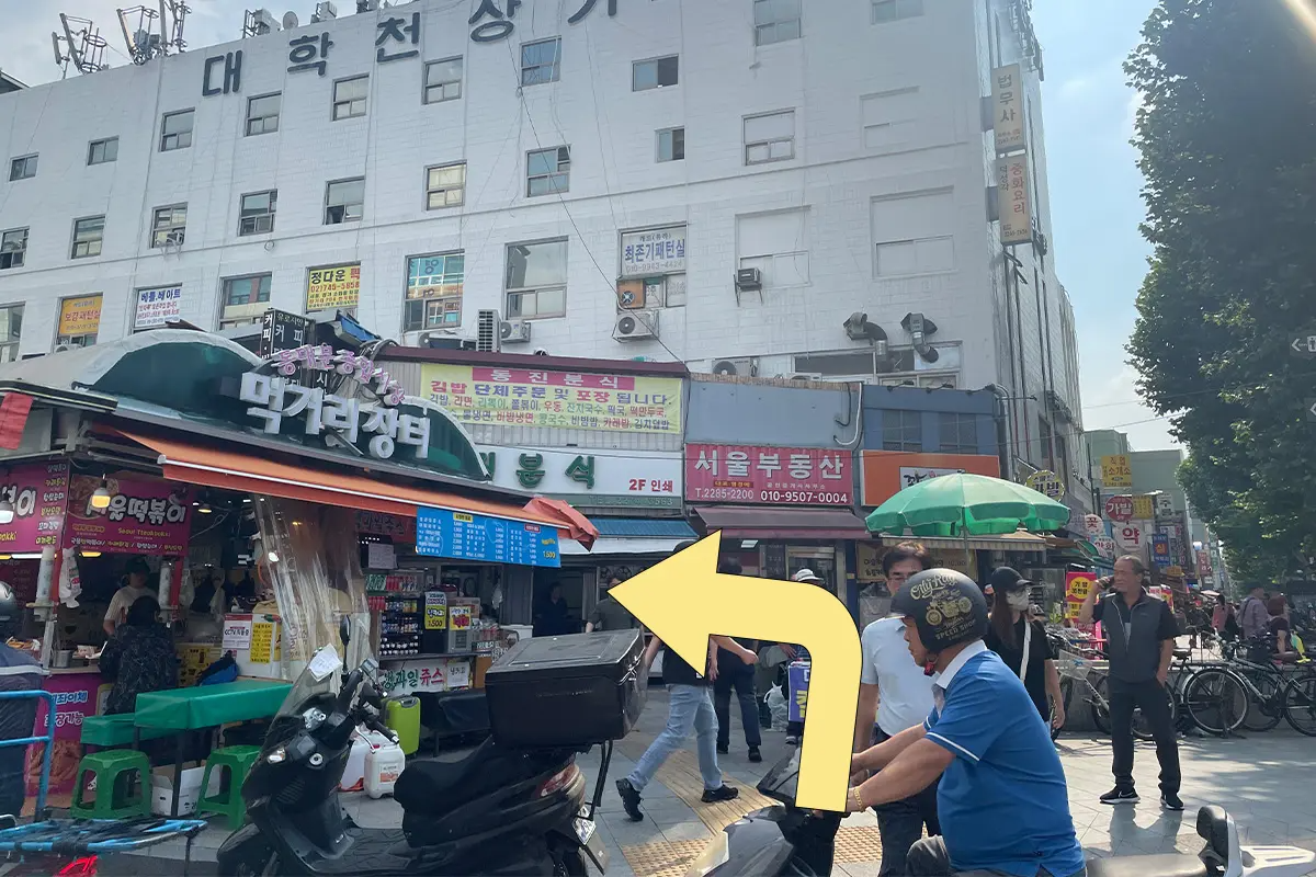 從東大門地鐵站出來後，拍攝的第一個街道場景，路邊有許多商店建築和行走的行人。