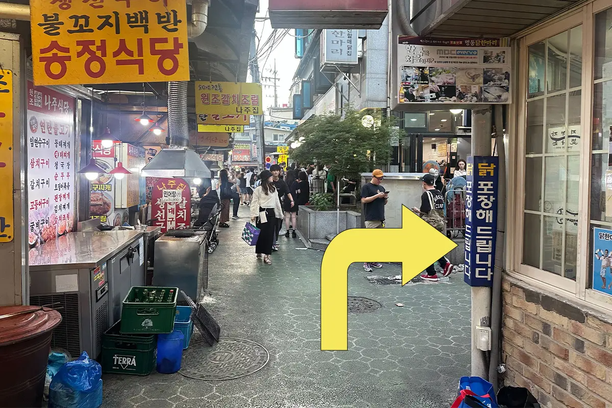 攤販間的其中一路徑直行指示圖，看到櫥窗裡面的店員和外頭的廣告招貼。