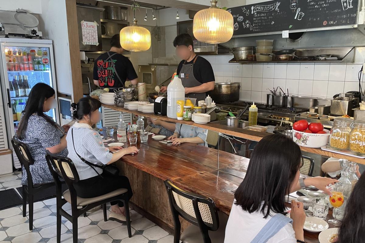 数名顾客在SAM SAM SAM餐厅内享用美食，展示开放式厨房和吧台的用餐气氛。