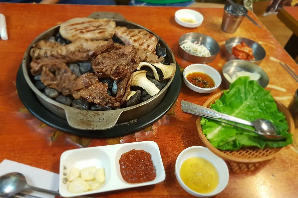 石の上で焼かれた美味しそうな韓国焼肉、サムギョプサルとキノコの盛り合わせ