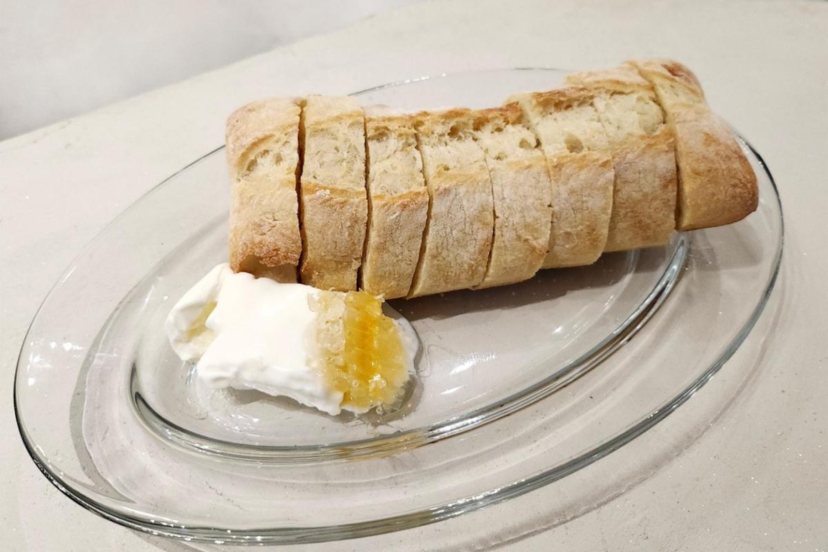 Frisch gebackenes Baguette mit cremigem Kaymak, serviert auf einem klaren Glas-Teller.