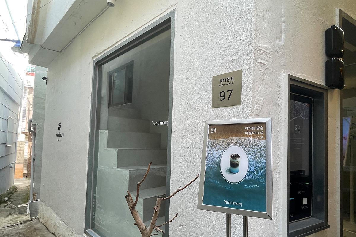 Weiß bemalter Eingang zum Hynyeoul Kulturdorf, geschmückt mit dem Yeoulmarq Logo.