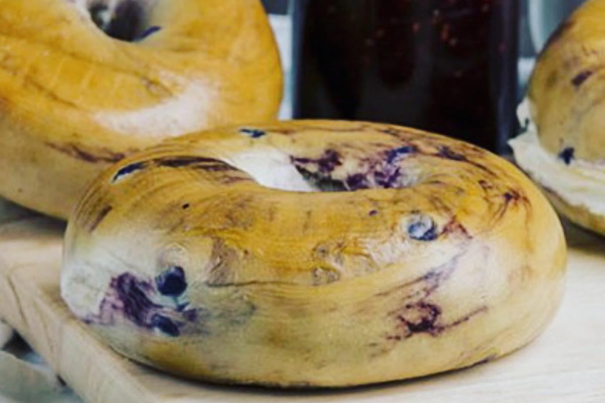 Zwei saftige Heidelbeer-Bagels auf einem Holzbrett arrangiert.