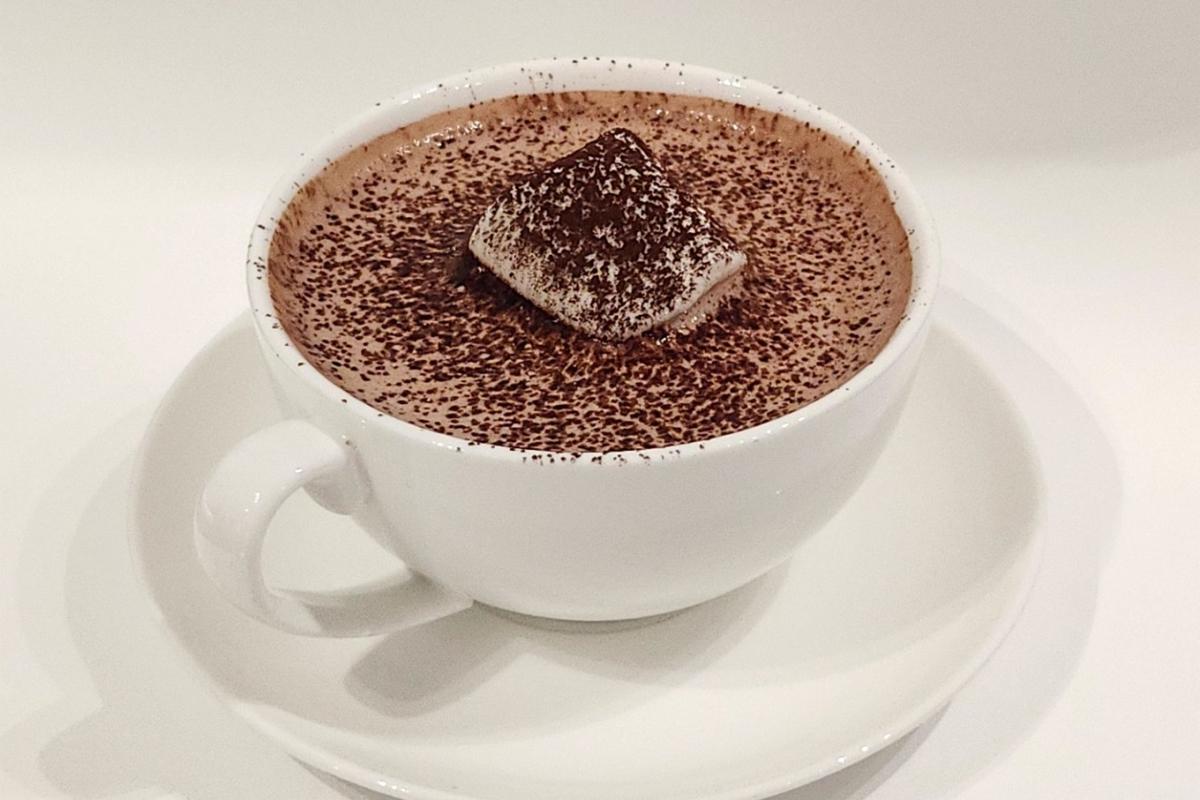 Eine Tasse schaumige, heiße Valrhona-Schokolade mit einem Spritzkuchen obendrauf.