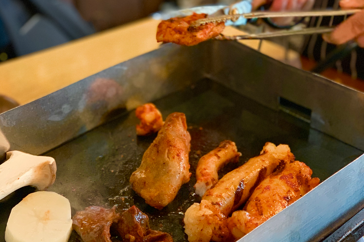 韓國烤腸在鐵板上烹煮，旁邊放置蔬菜與佐料