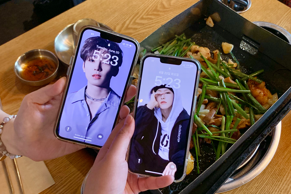 兩部手機顯示韓國偶像的屏保畫面，背景顯示餐桌上的燒腸和蔬菜