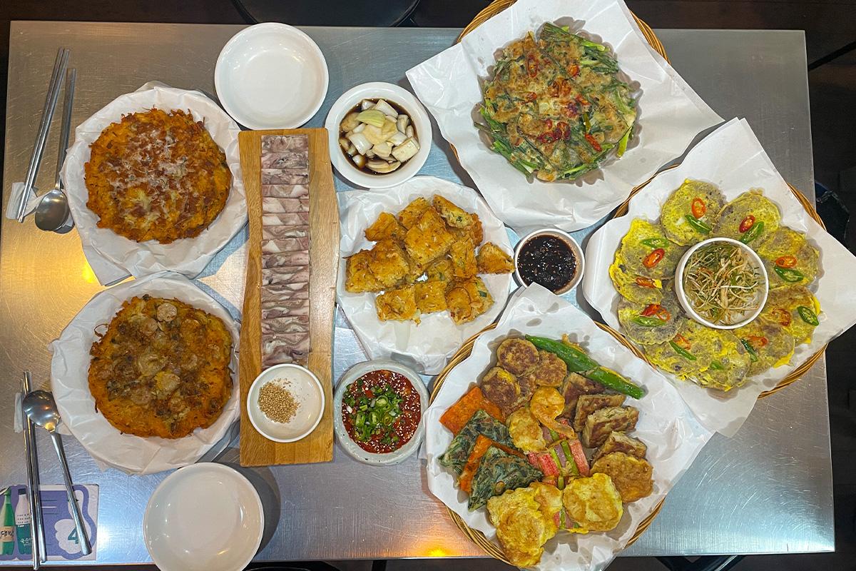 Verschiedene koreanische Pfannkuchen und Frühlingszwiebelsalat, serviert im Parkgane Bindaetteok auf dem Gwangjang-Markt, Seoul.