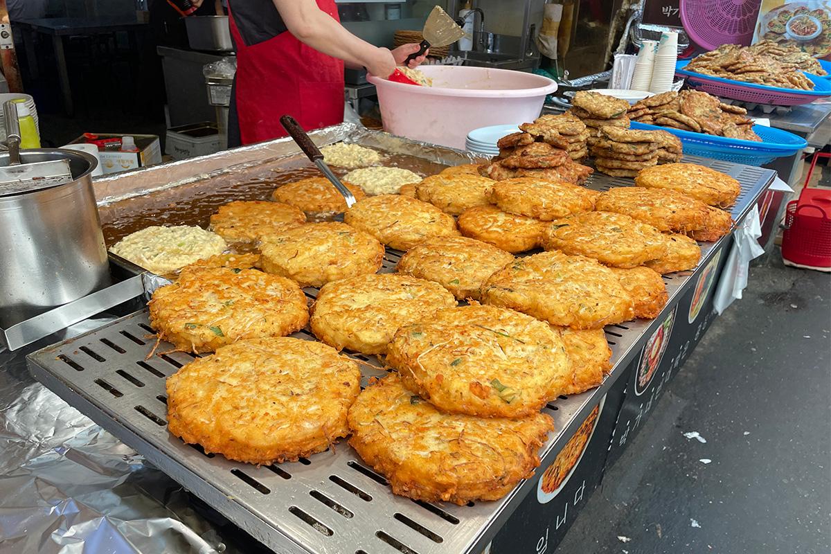 Ein Berg Bindaetteok auf einer Grillplatte, gekocht im Parkgane Bindaetteok auf dem Gwangjang-Markt in Seoul.